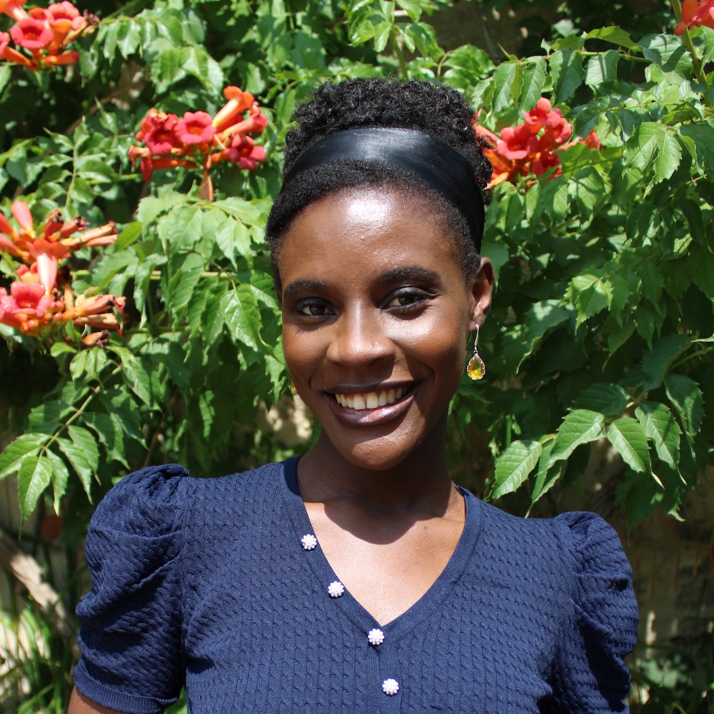 Person with neat tied back black hair, wearing a blue frilly top smiling at the camera.