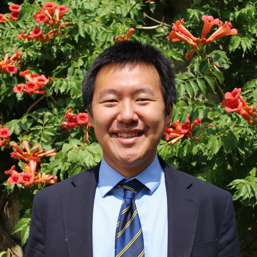 Person with short black hair wearing a dark suit, blue shirt and stripey tie, smiling at the camera.