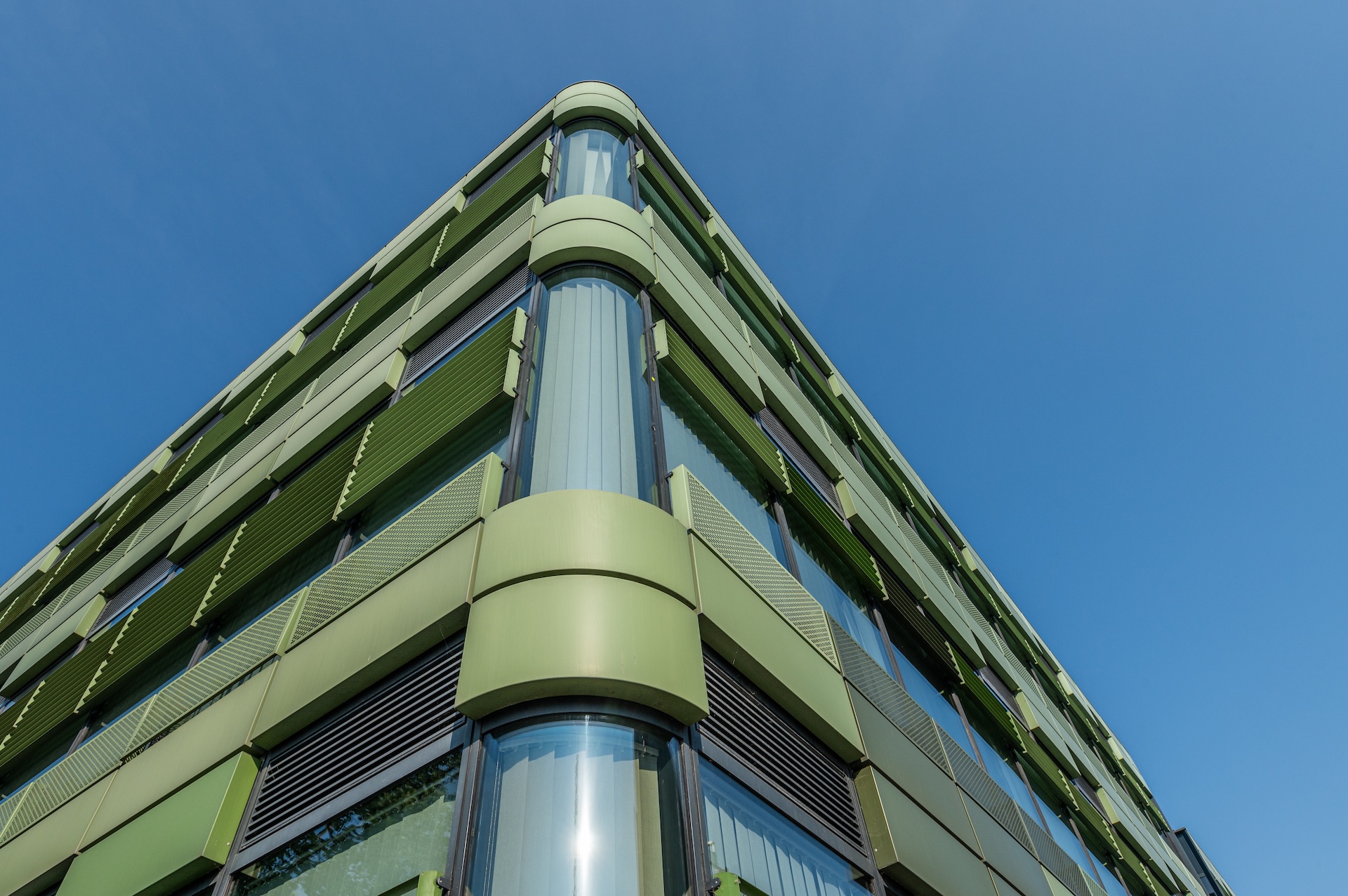 Corner of a modern university building with glass and green facade.