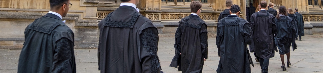 Line of Oxford students wearing formal black gowns walking in pairs towards a historical building.