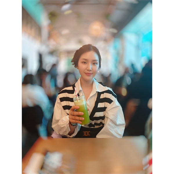 Portrait of person with short black hair, wearing a white and black stripy top, holding a green smoothie smiling at the camera