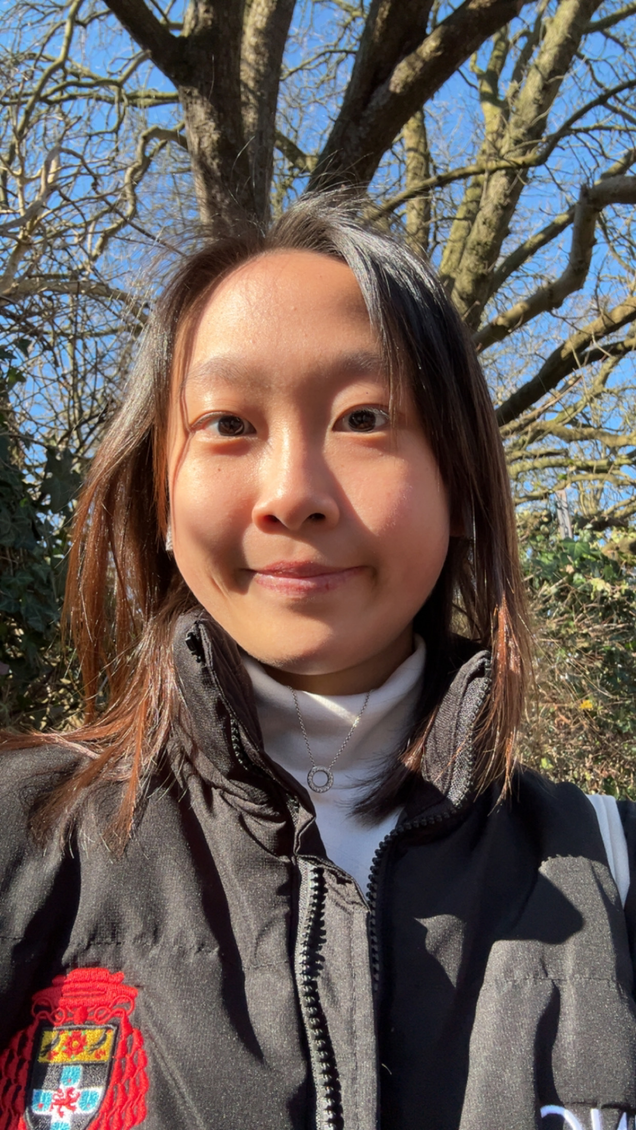 Person with long black hair standing outside with the sun shining on their face